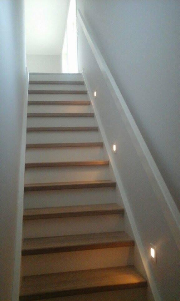 Schody drewniane z podświetleniem LED w ścianie, prowadzące do góry, widok od dołu.