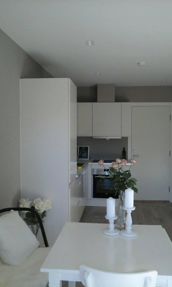 Jasne, minimalistyczne wnętrze kuchni z białymi meblami, stołem i dekoracjami kwiatowymi, oświetlenie sufitowe punktowe.