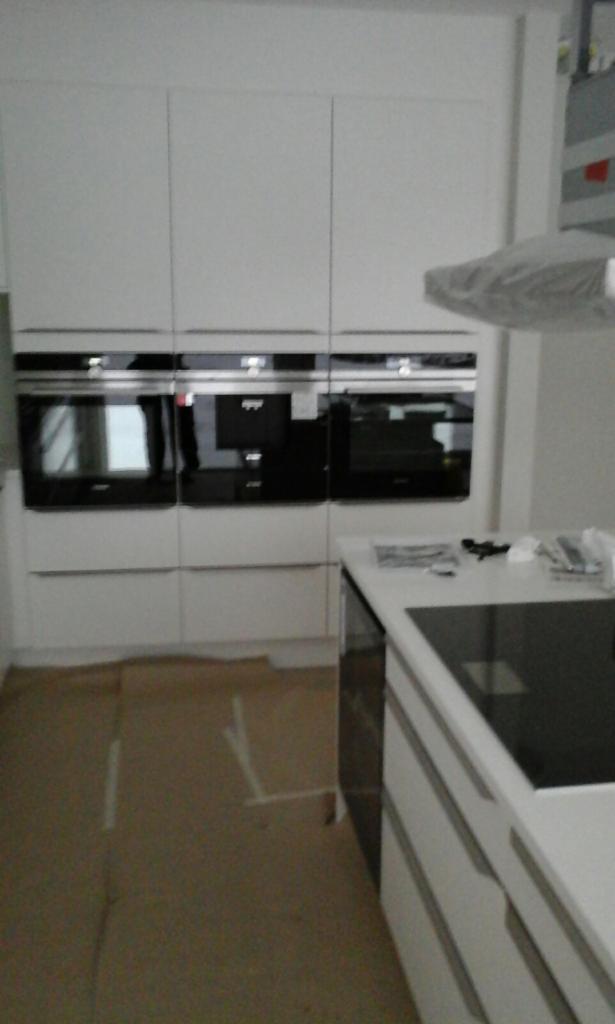 Nowoczesna, biała zabudowa kuchenna z trzema wbudowanymi piekarnikami, zabezpieczona podłoga tekturą falistą, okap kuchenny w folii ochronnej.