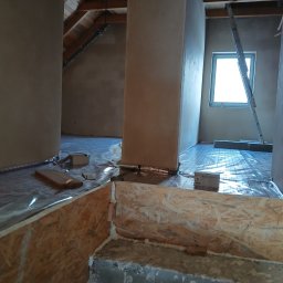 ART-INSTALBUD Artur Popowicz - Wnętrze poddasza w trakcie montażu ogrzewania podłogowego, widoczne rury grzewcze rozłożone na podłodze i przykryte folią, oraz fragment konstrukcji z płyty OSB z pianką montażową.