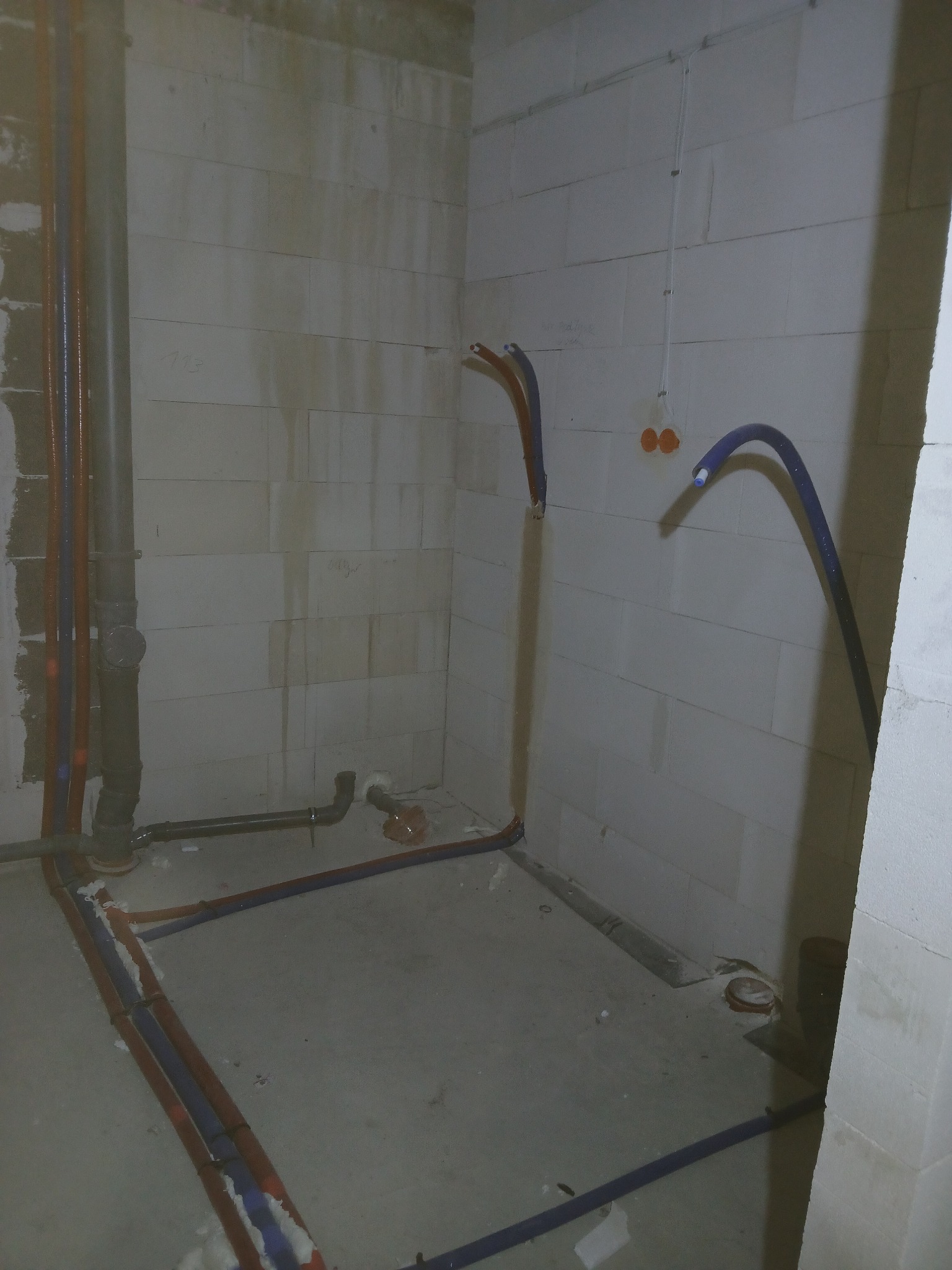 Surowy stan łazienki w trakcie instalacji: widoczne rury wodne i kanalizacyjne prowadzone po podłodze i ścianach z betonu komórkowego, przygotowane do dalszych prac wykończeniowych.