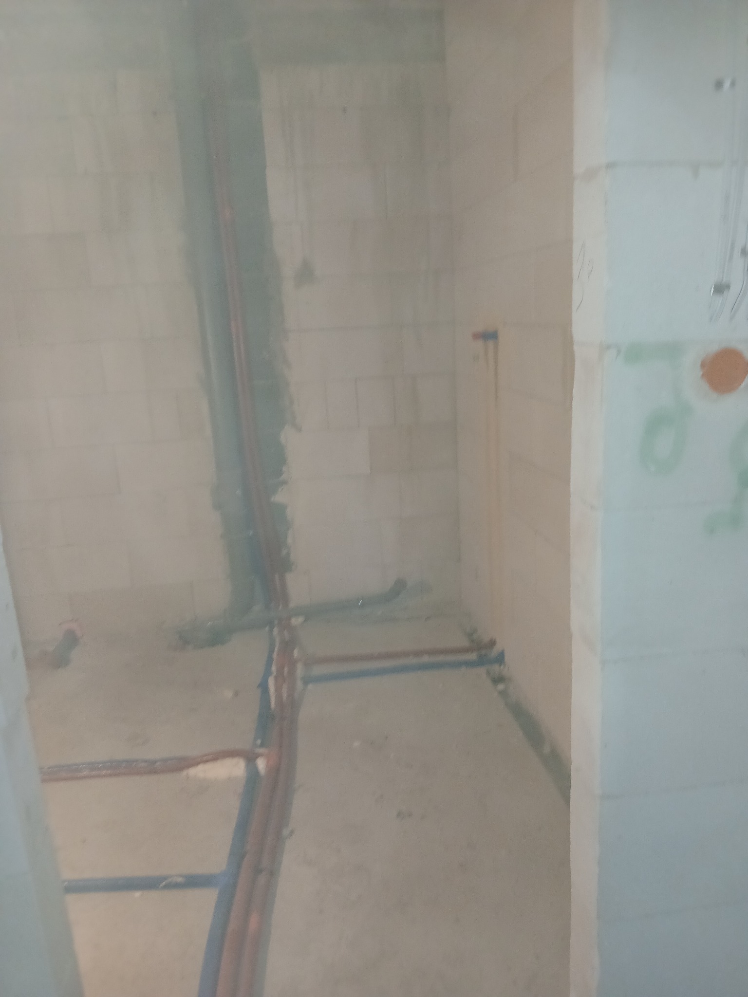 Surowy stan łazienki w trakcie prac hydraulicznych: widoczne pionowe i poziome rury instalacji wodnej i kanalizacyjnej w ścianach z betonu komórkowego, z zielonymi oznaczeniami na ścianie.