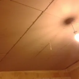 Sufit z płyt kartonowo-gipsowych, widoczne łączenia i wkręty, oświetlony żarówką wiszącą na kablu.