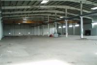 Wnętrze hali produkcyjnej w trakcie budowy z widoczną konstrukcją stalową dachu, surową posadzką i kolumnami. Niedokończony stan obiektu.