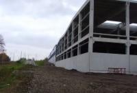 Surowy, betonowy szkielet budynku w trakcie budowy, widok z dołu, pochmurne niebo w tle. Widoczne zbrojenia i elementy konstrukcyjne.