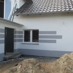 Biała elewacja domu z szarymi poziomymi pasami, widoczne okno, drzwi wejściowe i sterta ziemi.