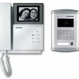 Zestaw wideodomofonowy z kolorowym ekranem LCD, biała obudowa, widok na panel zewnętrzny, zbliżenie na zdjęcie dwóch uśmiechniętych osób na monitorze.