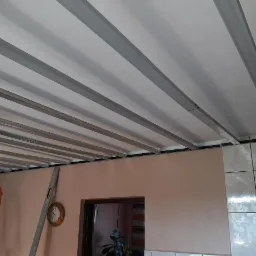 Montaż stelażu pod płytę karton gips na suficie, widoczne profile metalowe, ściana pomalowana na różowo, fragment kafelków.