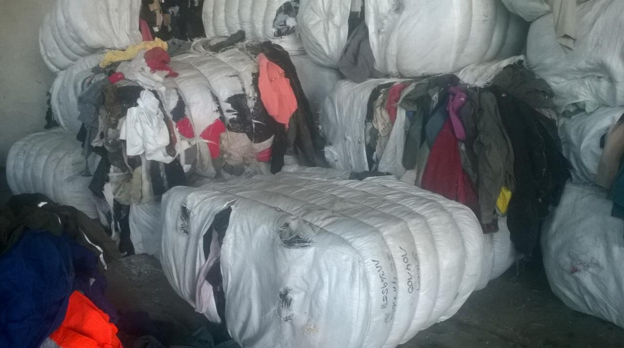 Stos sprasowanej odzieży używanej w białych workach, widoczne fragmenty ubrań w różnych kolorach. Nieostre zdjęcie.