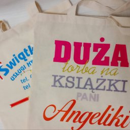 DPCOLOR - Dwie beżowe torby bawełniane z kolorowymi nadrukami: jedna z logo firmy 'Świątl', druga z napisem 'DUŻA torba na KSIĄŻKI PANI Angeliki' w różnych kolorach.