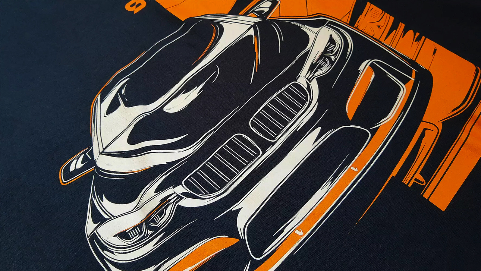 Czarna koszulka z nadrukiem graficznym przedstawiającym fragment samochodu w kolorach pomarańczowym i białym, widoczne detale reflektorów i grilla.