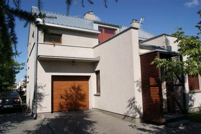 Nowoczesny dom jednorodzinny z garażem i drewnianą osłoną wejścia, widok z zewnątrz w słoneczny dzień.