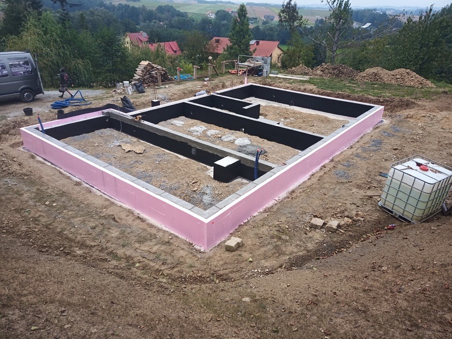 Fundamenty domu jednorodzinnego z izolacją termiczną w kolorze różowym, widok z góry na działce z widokiem na okoliczne domy i las