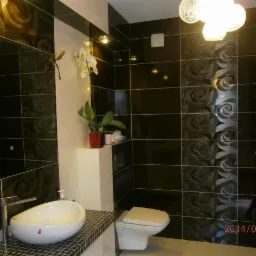 Czarno-biała łazienka z umywalką nablatową, toaletą wiszącą i dekoracyjną ścianą z motywem róż, oświetlona nowoczesną lampą.