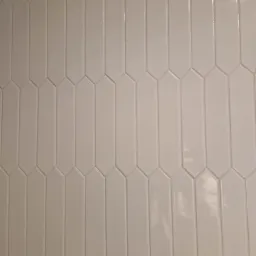 Beżowe, podłużne, błyszczące płytki ułożone pionowo, z delikatnymi fugami, tworzące wzór na ścianie.