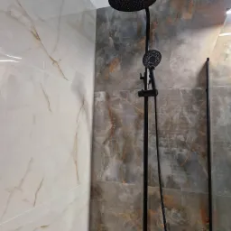 Nowoczesna łazienka z czarną deszczownicą i panelami ściennymi imitującymi marmur w odcieniach szarości i beżu.