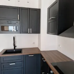 Nowoczesna kuchnia z czarnymi szafkami i drewnianym blatem, czarny zlew z wysoką baterią, oświetlenie punktowe, płyta indukcyjna