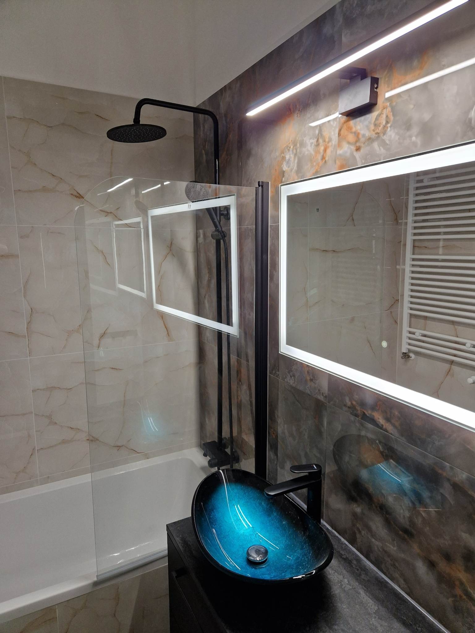 Nowoczesna łazienka z umywalką w kolorze turkusowym, czarną armaturą, kabiną prysznicową ze szklanym panelem i podświetlanym lustrem.