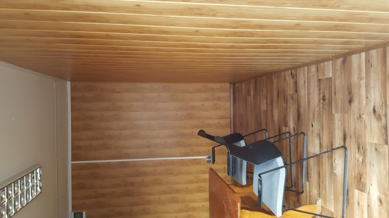 Wykończenie wnętrza pomieszczenia panelami imitującymi drewno na ścianach i suficie, z widocznym fragmentem metalowej konstrukcji i krzesła.