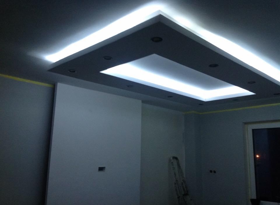 Nowoczesny sufit podwieszany z oświetleniem LED w kształcie prostokąta, szare ściany, widoczna drabina, okno. Element wykończenia wnętrza.