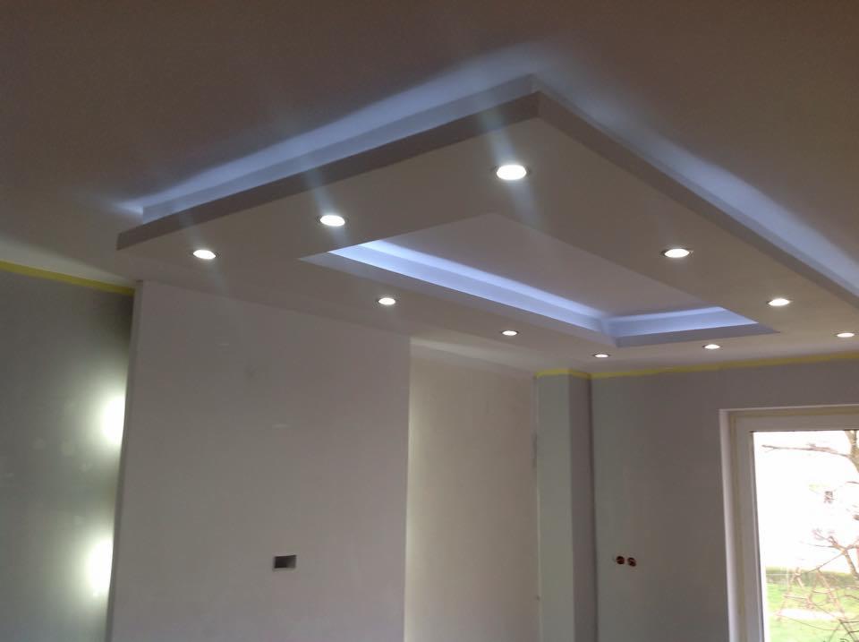 Podwieszany sufit z oświetleniem punktowym i ledowym w nowocześnie wykończonym wnętrzu. Żółta taśma malarska na ścianie sygnalizuje etap prac.