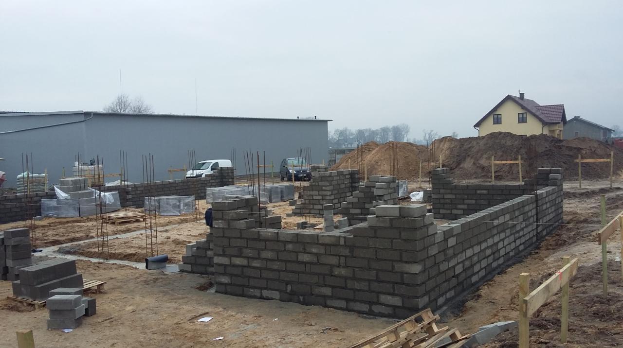 Wznoszenie ścian fundamentowych z bloczków betonowych na placu budowy domu jednorodzinnego. Widoczne zbrojenia i przygotowane materiały.
