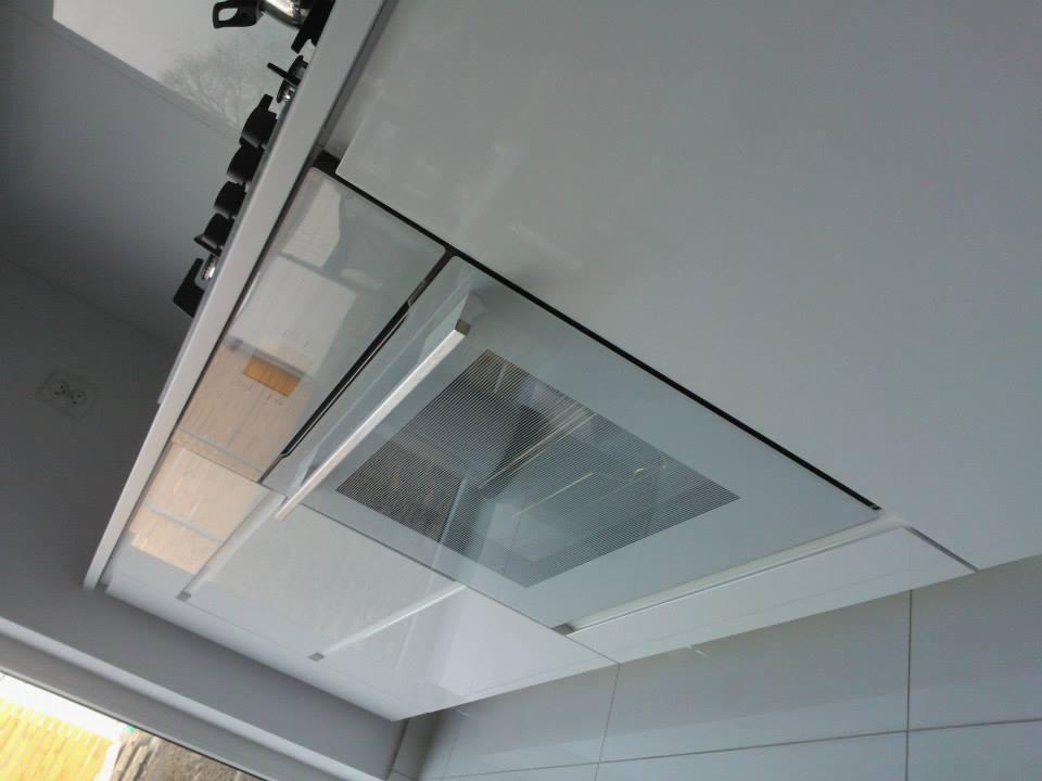 Biała zabudowa kuchenna z piekarnikiem i płytą grzewczą, widok z dołu, nowoczesny design, minimalistyczne wykończenie, jasne wnętrze, gładkie fronty szafek.