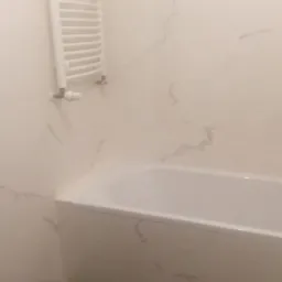 Wykończona łazienka z wanną, grzejnikiem drabinkowym i ciemną podłogą. Ściany wyłożone płytkami imitującymi marmur.