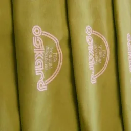 Rząd oliwkowych koszulek z identycznym, jasnoróżowym nadrukiem 'Tyska Spółdzielnia Mieszkaniowa' w pionowym układzie na każdej z nich.