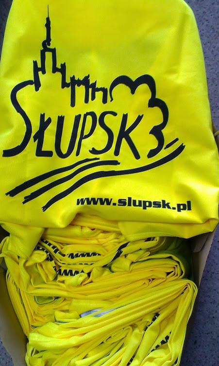 Żółte koszulki z czarnym nadrukiem 'Słupsk' i sylwetką miasta, ułożone w kartonowym pudełku.