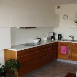 Nowoczesna kuchnia z białymi szafkami górnymi i drewnianymi dolnymi, z blatem w kolorze bieli. Widoczny zlew, płyta indukcyjna i dekoracje.