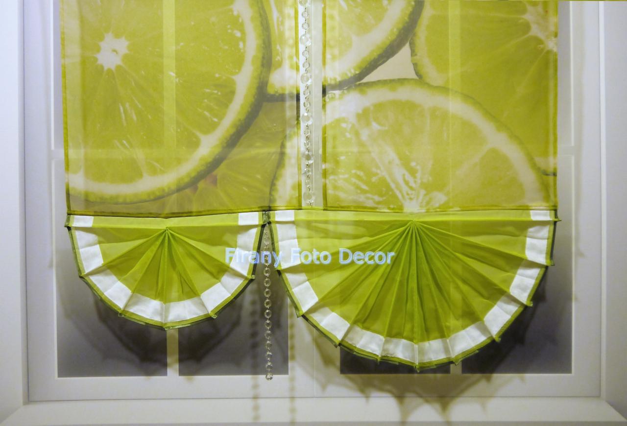 Żółto-zielona roleta rzymska z motywem cytryny, wykończona białymi elementami i ozdobnym łańcuszkiem, w białej ramie. Dekoracja okna w nowoczesnym stylu.
