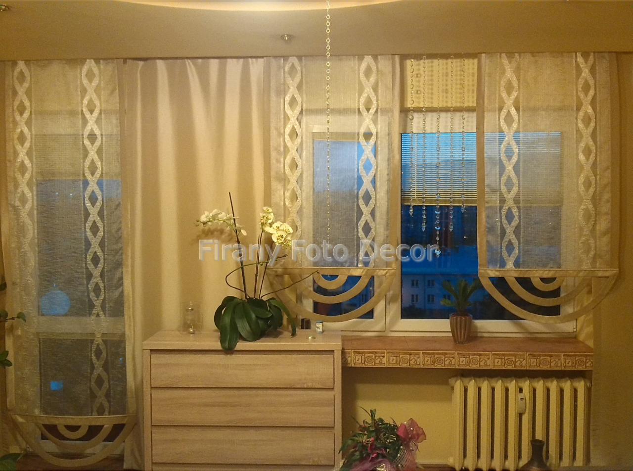Beżowe zasłony rzymskie z dekoracyjnym wzorem, kwiaty na komodzie. Widok na okno z żaluzjami i dekoracyjnym lambrekinem. Ciepłe oświetlenie wnętrza.