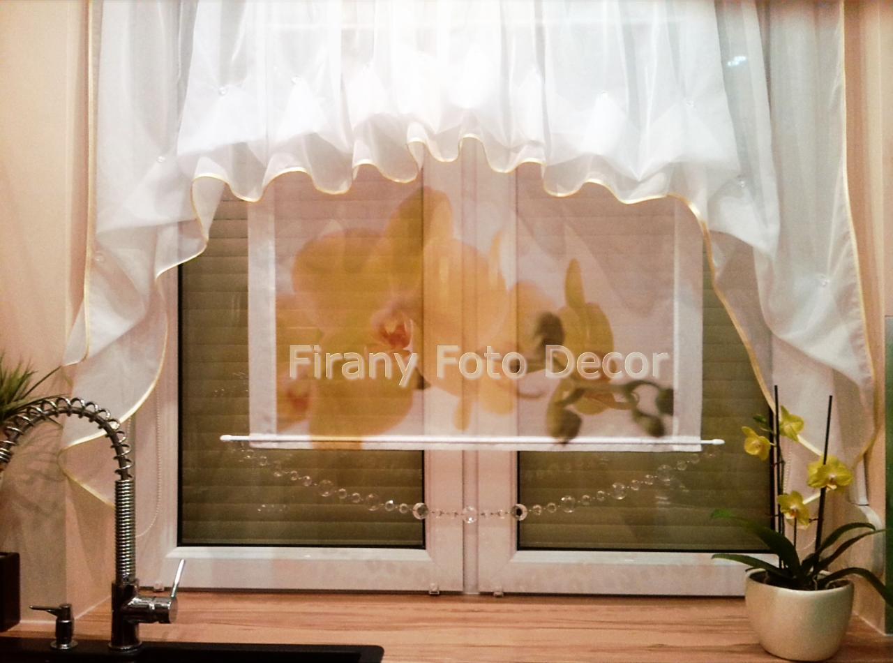 Delikatna, biała zasłona z falbanką i złotą lamówką, zawieszona nad oknem z roletą i dekoracją z koralików. W tle widoczny motyw kwiatowy.