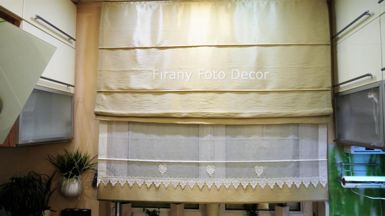 Beżowa roleta rzymska z koronkowym wykończeniem w kuchni, widoczna na tle szafek i roślin doniczkowych. Delikatne światło podkreśla fakturę materiału.