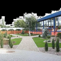 Widok na zadbany ogród z ścieżką z kamienia prowadzącą do budynku z dużymi oknami. W tle ogrodzenie z cegły z białymi łukami.