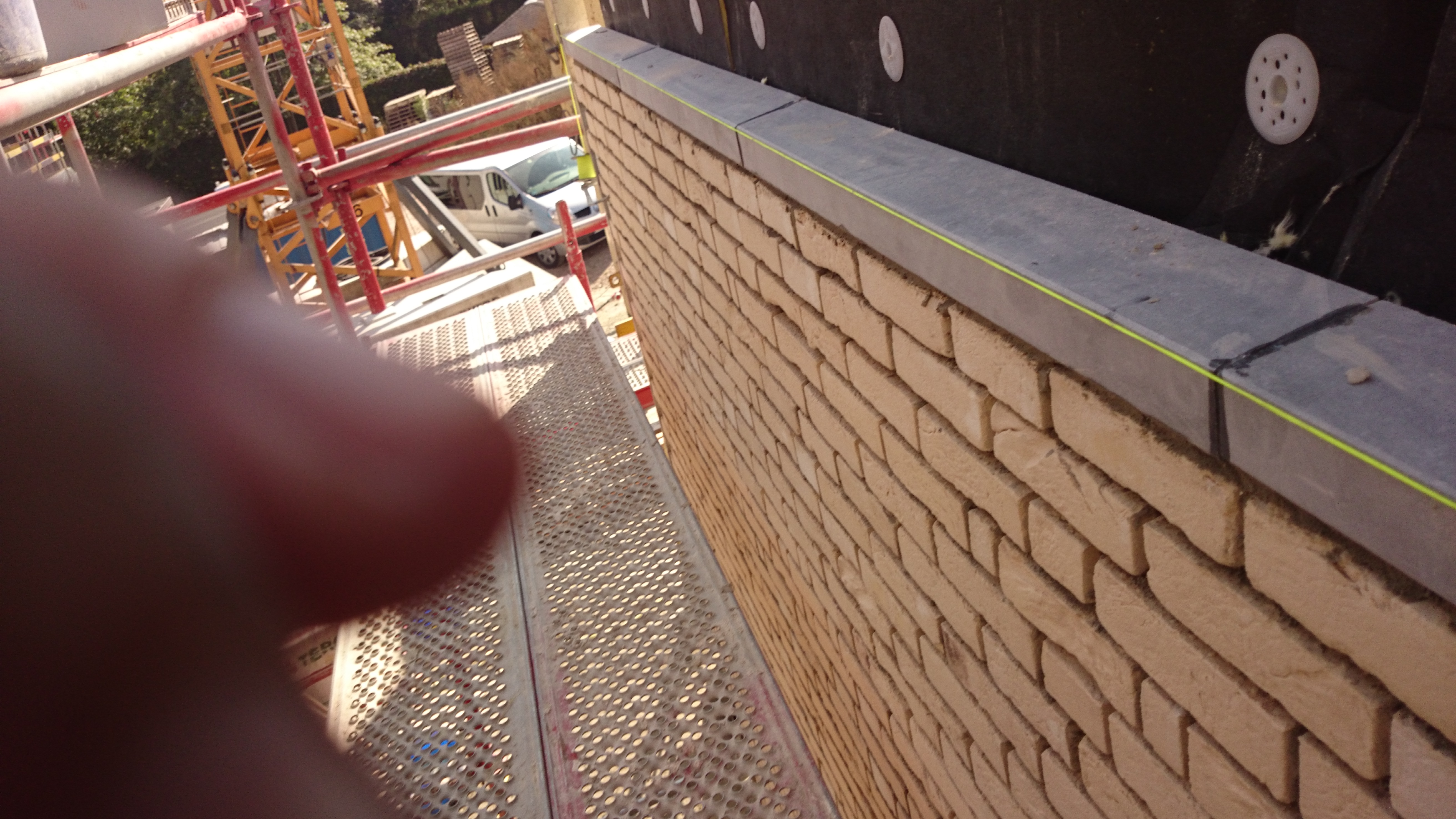 Ściana z cegły klinkierowej z widocznym rusztowaniem i elementami izolacji. Uwagę zwraca precyzyjne wykonanie i estetyczne połączenie materiałów.