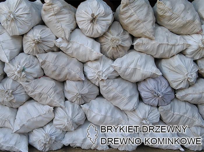 Stos worków z zawiązanymi górnymi brzegami, prawdopodobnie zawierających materiał opałowy, ułożonych jeden na drugim, tworzących ścianę. Jeden worek ma lekko szary odcień. Na dole widoczny napis...