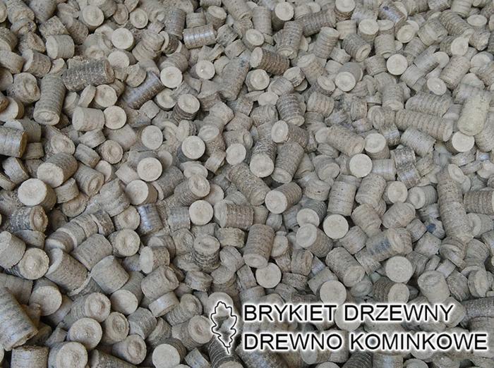 Stos cylindrycznych brykietów drzewnych o widocznej strukturze włókien, ułożonych chaotycznie, wypełniających całą klatkę zdjęcia.