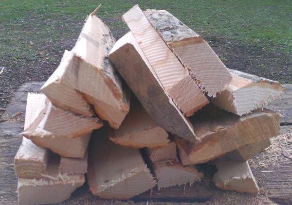 Stos pociętego, jasnego drewna na tle trawy, ukazujący strukturę słojów. Drewno ułożone na drewnianej powierzchni, widoczne drobne wióry.