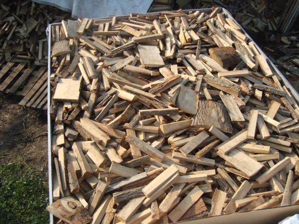 Klatka wypełniona pociętym drewnem opałowym, widoczne kawałki kory i jasne drewno, zróżnicowane kształty i rozmiary, ułożone bezładnie w metalowej skrzyni.