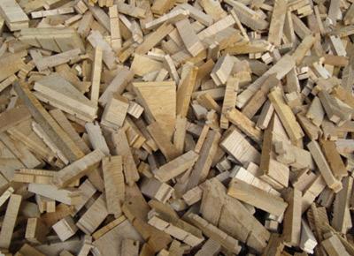 Stos pociętych kawałków drewna o jasnej barwie, różnej wielkości i kształtach, ułożonych chaotycznie. Widoczne sęki i struktura drewna.