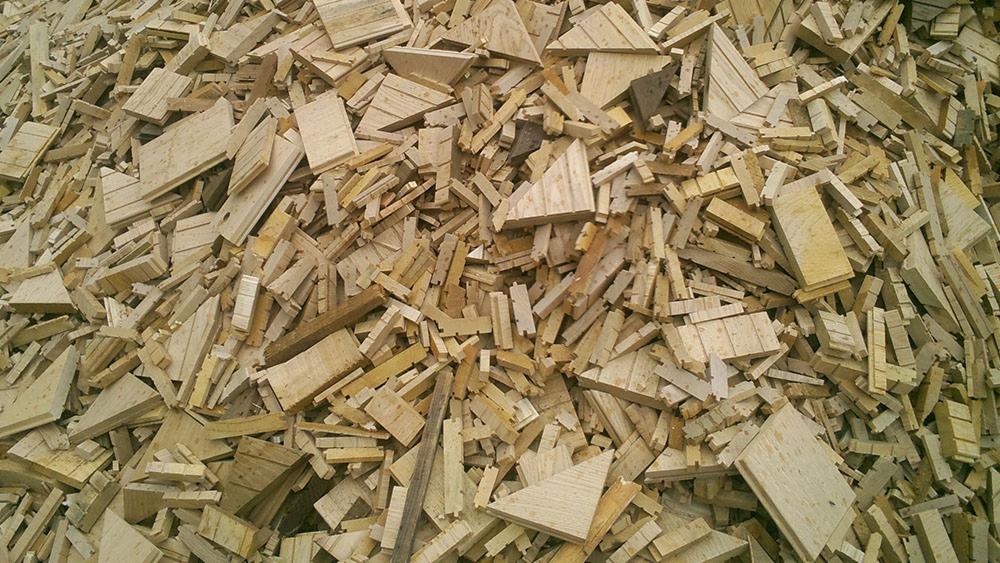 Góra pociętych, jasnych desek i listew drewnianych o różnych kształtach, tworzących chaotyczną, ale uporządkowaną stertę. Widok z góry, naturalne oświetlenie.