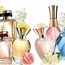 Kolekcja flakonów perfum Avon w różnych kształtach i kolorach, ozdobiona białymi i żółtymi kwiatami oraz różą.