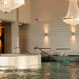 Luksusowe wnętrze basenu z jacuzzi, wykończonego mozaiką. Oświetlenie punktowe i kryształowe żyrandole. Elementy dekoracyjne z kamienia. Schody z poręczami.