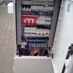 E-funia Projekty techniczne, Automatyka przem., Elektryka, kompensacja mocy biernej, Falownikowe Układy Napędowe - Otwarta skrzynka elektryczna z widocznymi bezpiecznikami, przewodami i elementami instalacji. Widoczne zabezpieczenia przepięciowe. Instalacja w białej obudowie.