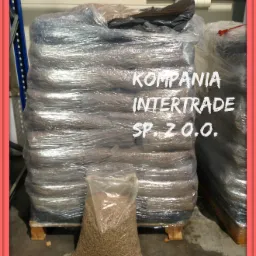 Paleta z pelletem owinięta folią stretch, obok worek z pelletem. Widoczny napis 'Kompania Intertrade Sp. z o.o.'. Magazynowe tło.