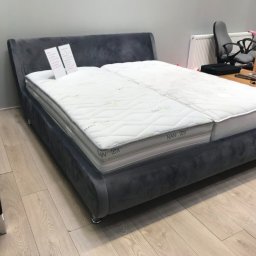 Design 4 Beds Sp. zo.o. - Szare, tapicerowane łóżko z dwoma materacami o różnym stopniu zużycia, w tle biuro z krzesłami.