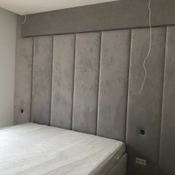 Design 4 Beds Sp. zo.o. - Szary tapicerowany zagłówek łóżka z panelami pionowymi, widoczne gniazdka elektryczne i wystające kable, łóżko z materacem w folii ochronnej.
