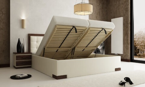 Beżowe łóżko tapicerowane z podnoszonym stelażem i pojemnikiem na pościel, widok na drewniany stelaż i mechanizm podnoszenia, szafka nocna z wazonami w tle.